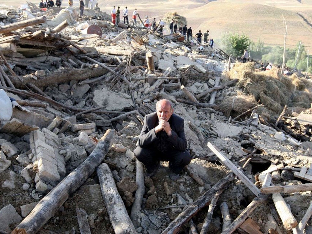 An Iranian resident from the village of Baje-Baj, near the town of Varzaqan, stands on top of the rubble of his destroyed home