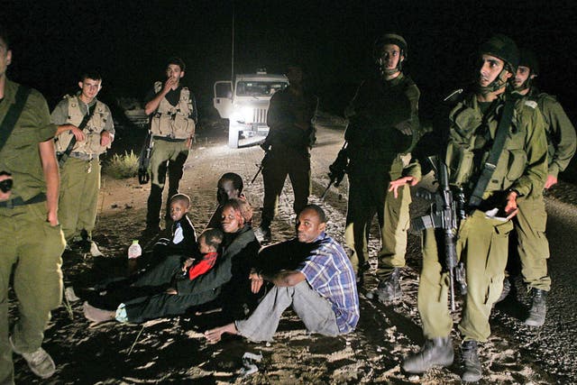 Sudanese refugees sit on the ground surrounded by Israeli soldiers after crossing illegally from Egypt into Israel