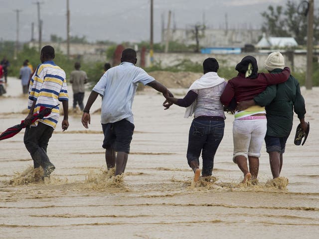 People help each other across a flooded section of a road in Port-au-Prince
