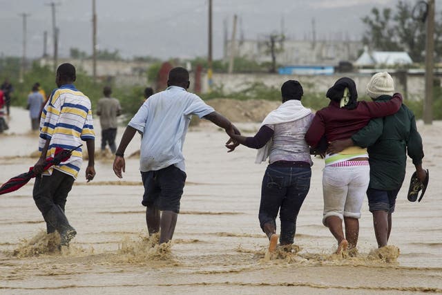 People help each other across a flooded section of a road in Port-au-Prince