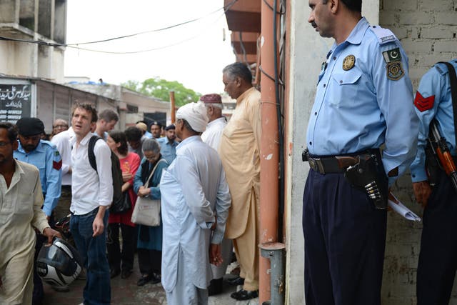 Pakistani policemen keep watch as minority Christians and journalists gather outside the court building during the case hearing