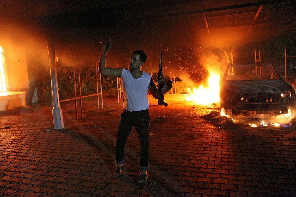 An armed man waves his rifle as buildings and cars are engulfed in flames after being set on fire inside the US consulate compound in Benghazi late on September 11, 2012.