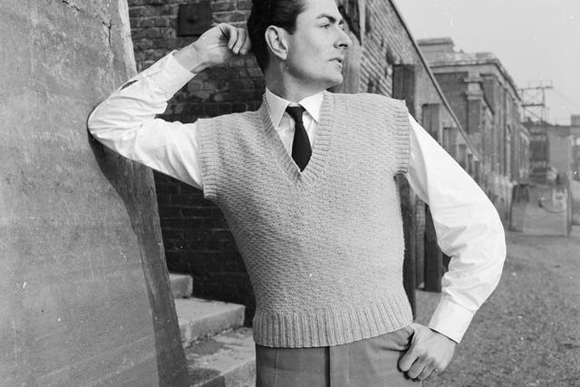 13th January 1958: A man wearing a woollen V-neck pullover accentuating his shirt and tie leans ostentatiously on the wall of a back street. Woman's Illustration