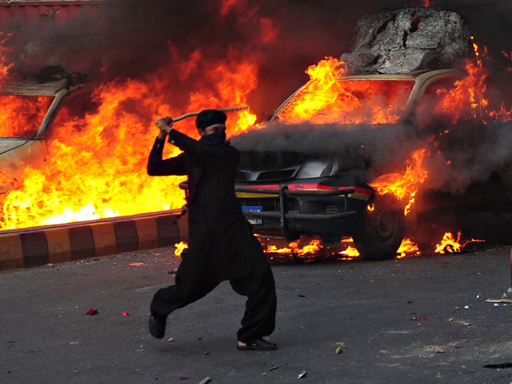 A Pakistani Muslim demonstrator brandishes a stick near burning police vehicles during a protest against an anti-Islam film in Karachi