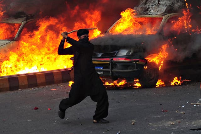 A Pakistani Muslim demonstrator brandishes a stick near burning police vehicles during a protest against an anti-Islam film in Karachi