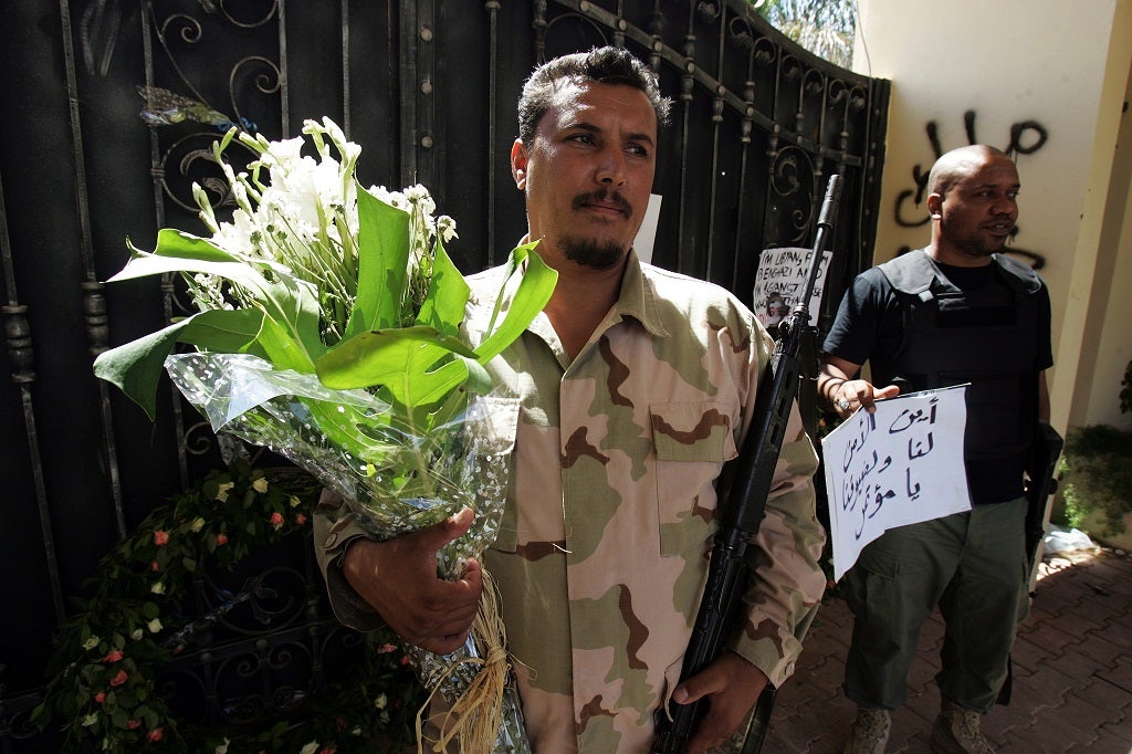 Libyan security guards hold flowers and slogans left by people protesting against last week's attack, in which ambassador Chris Stevens died, at the main entrance of the US consulate in Benghazi