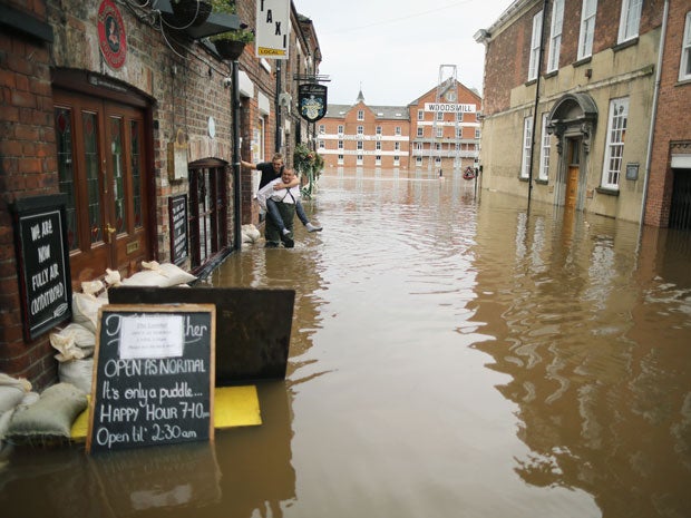 A man carries a a freind through floodwaters as the swell of the River Ouse flows through the city of York