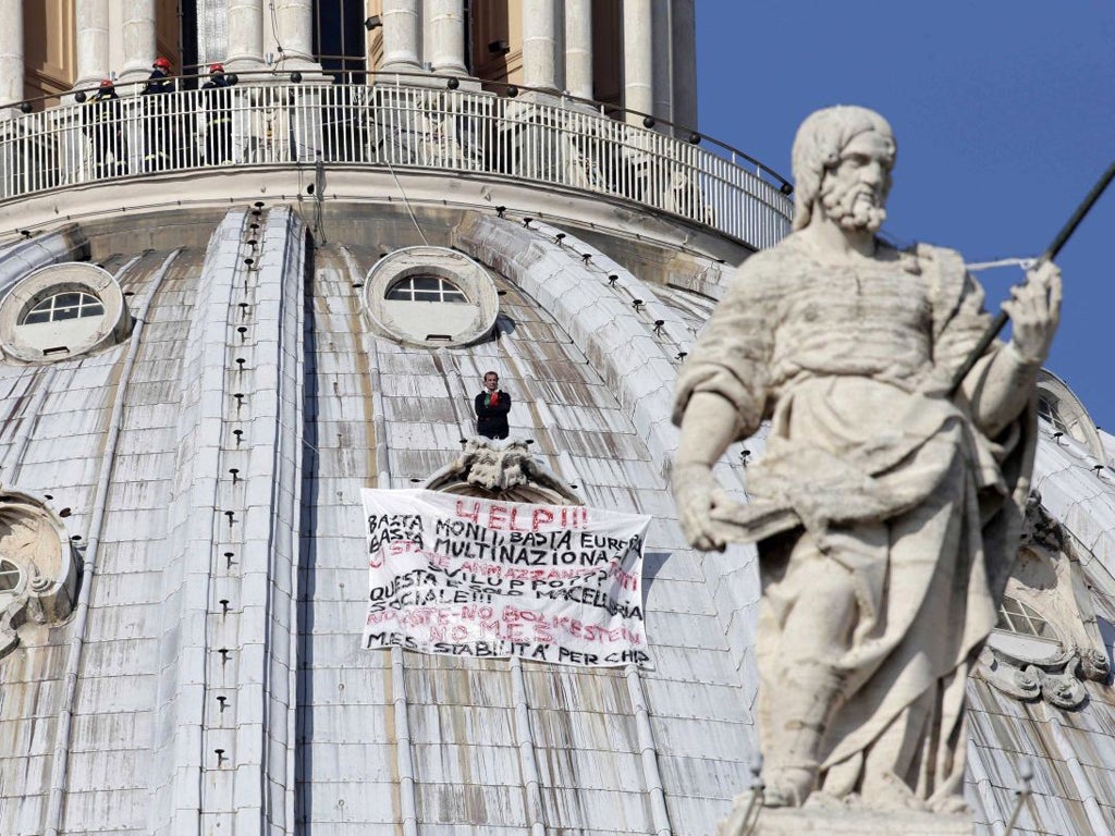 Firefighters look at Italian businessman Marcello di Finizio standing above his banner which reads in Italian "Help!! Enough Monti (Italian Premier Mario Monti), enough Europe, enough multinationals, you are killing all of us. Development?? This is a social butchery!!", as he protests on St. Peter's 130-meter-high (42-feet-high) dome