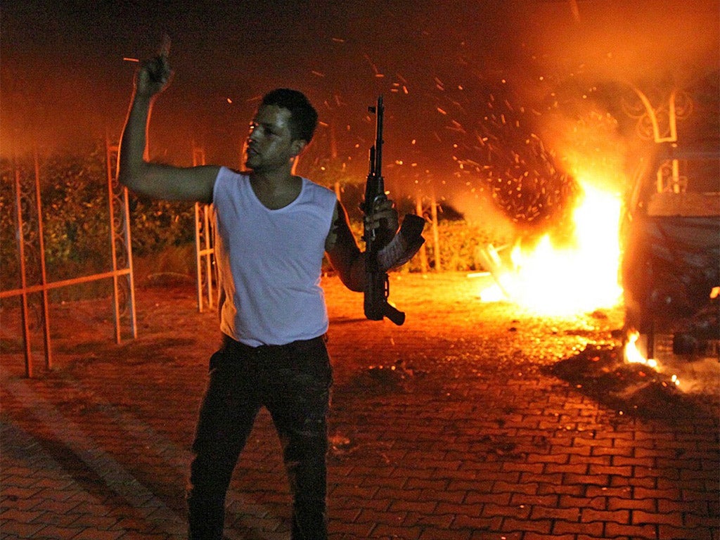 An armed man waves his rifle as buildings and cars are engulfed in flames after being set on fire inside the US consulate compound in Benghazi last month