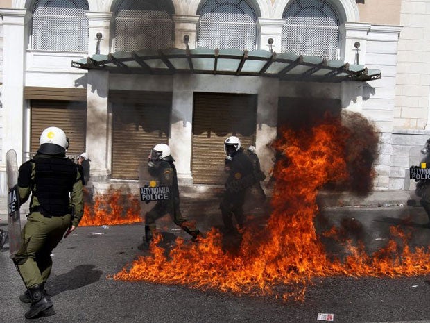 Riot police stand in front of flames caused by a molotov cocktail during clashes at the demonstration in Athens