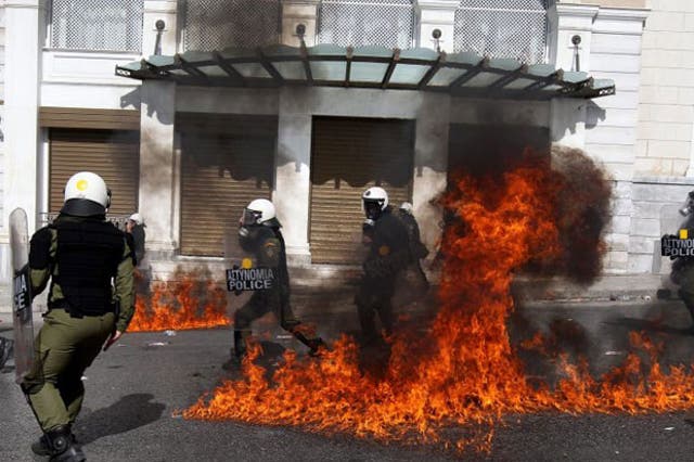 Riot police stand in front of flames caused by a molotov cocktail during clashes at the demonstration in Athens
