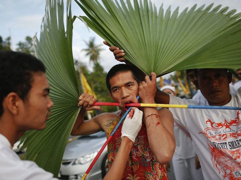 A devotee of Ban Tha Rua Chinese shrine with knives pierced through his cheeks takes part in a procession celebrating the annual vegetarian festival in Phuket