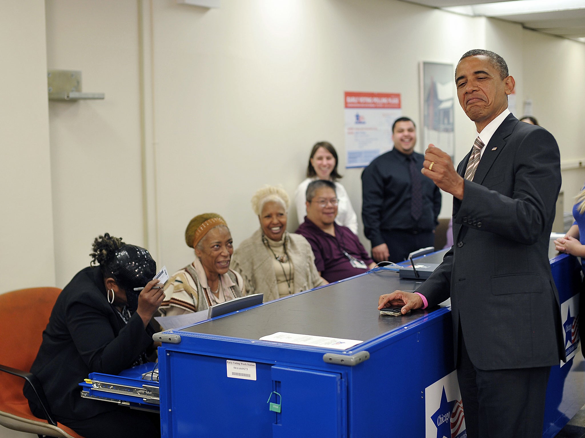 Barack Obama jokes with election worker Marie Holmes (left) who double-checked his photo on his driver's licence as he signed in for early voting in Chicago