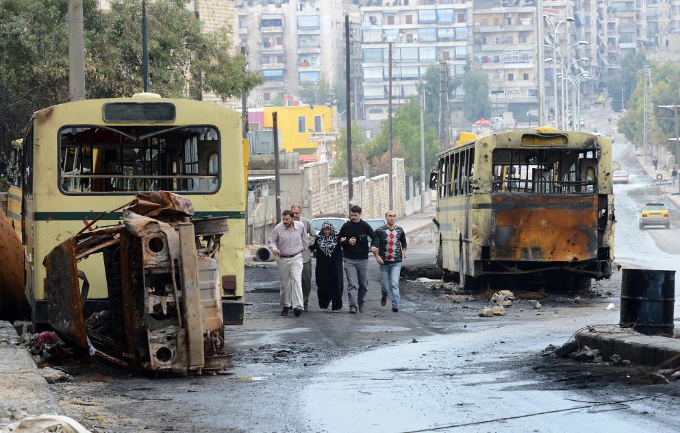 Syrian civilians walk past burnt buses near a checkpoint in the northern city of Aleppo. Outbursts of fighting threatened to undermine a fragile ceasefire that took effect in Syria after President Bashar al-Assad's regime and the main rebel force agreed t