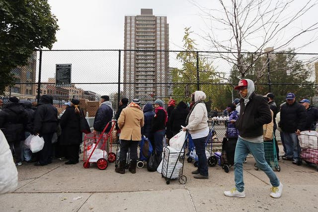 A man walks past as people line up to receive free necessities at a distribution point outside public housing units in Manhattan’s East Village following Superstorm Sandy