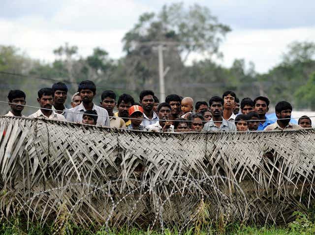 Sri Lankan war-displaced civilians peer from behind barbed wire fences surrounding their internment camp in Vavuniya