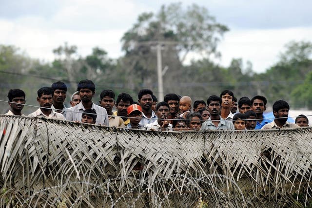Sri Lankan war-displaced civilians peer from behind barbed wire fences surrounding their internment camp in Vavuniya