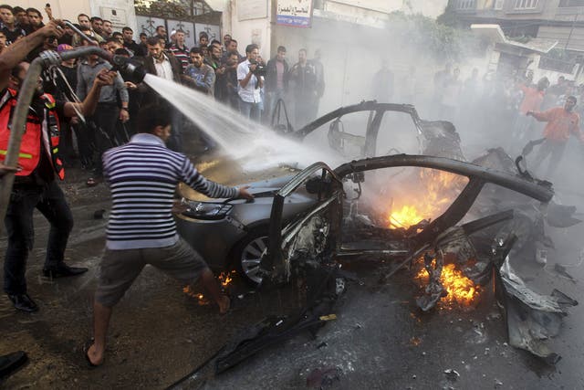 Palestinians extinguish fire from the car of Ahmed al-Jabari after it was hit by one of several Israeli air strikes in Gaza City