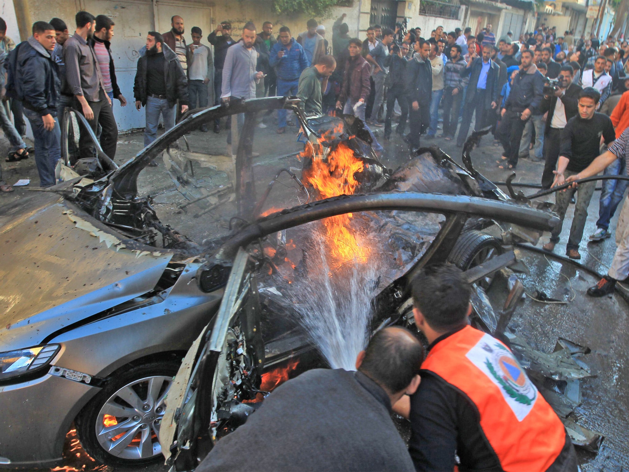 Palestinians extinguish fire from the car of Ahmed al-Jabari after it was hit by one of several Israeli air strikes in Gaza City