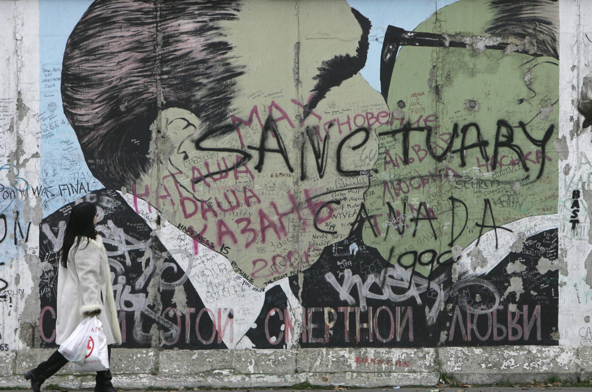 A picture taken 09 December 2004 shows a woman walking past a depiction of the now famous kiss between Soviet leader Leonid Brezhnev (L) and east German leader Erich Honecker at so-called East Side Gallery, a 1,3 km-long portion of the Berlin wall.