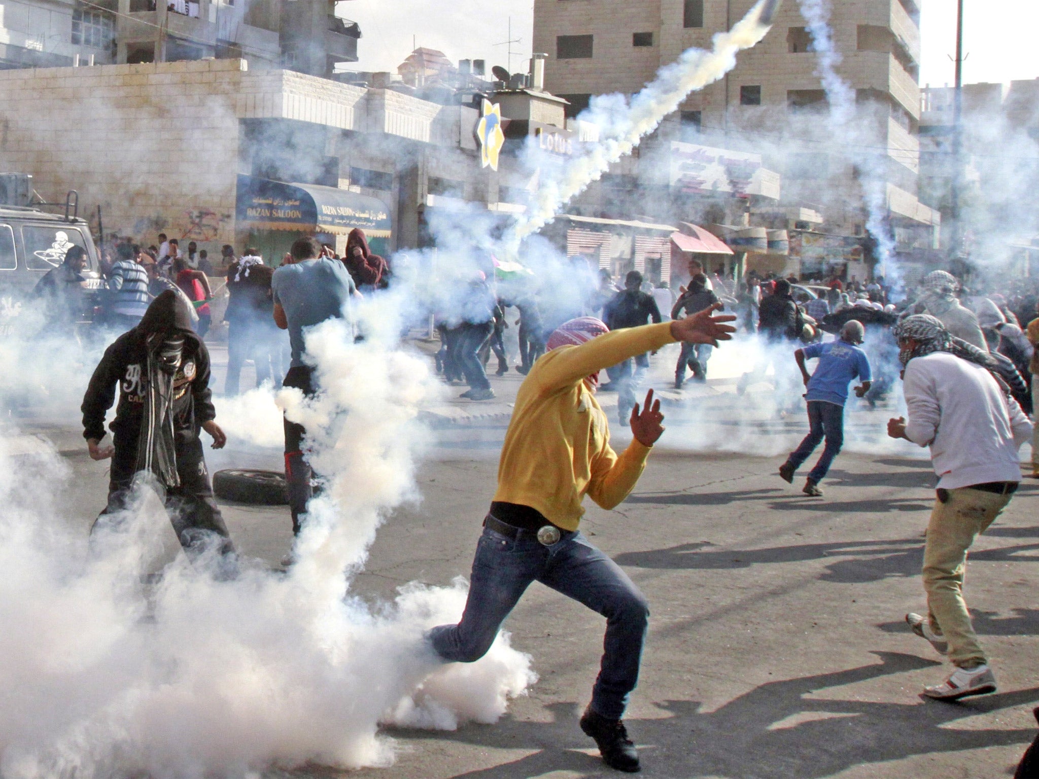A masked Palestinian youth throws back a tear gas canister towards Israeli security forces