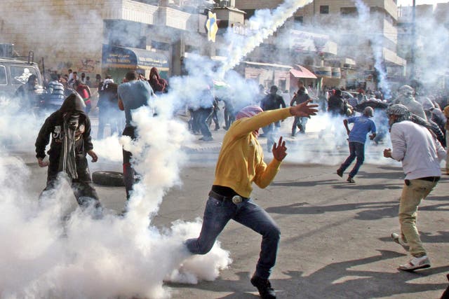A masked Palestinian youth throws back a tear gas canister towards Israeli security forces