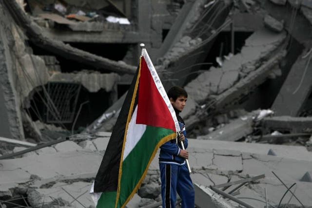 A Palestinian boy carries the national flag as he makes his way through the debris of the destroyed Palestine Sports Stadium in Gaza City