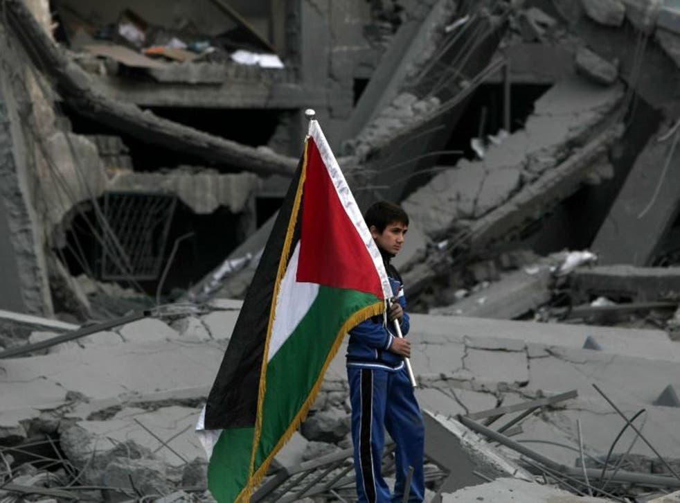 A Palestinian boy carries the national flag as he makes his way through the debris of the destroyed Palestine Sports Stadium in Gaza City