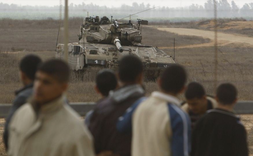 Palestinians stand close to the fence as an Israeli tank is seen on the border between Israel and southern Gaza Strip