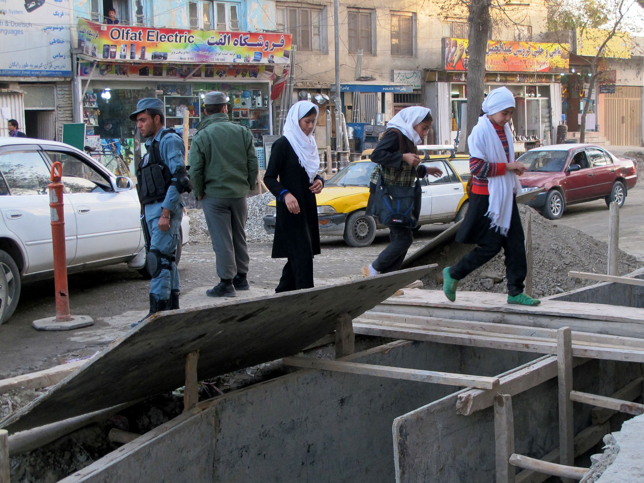 AFGHAN: School children in Kabul, Afghanistan, cross a plank over a newly dug drainage ditch on Nov. 14. A major road construction project has created havoc in the capital of 5 million.