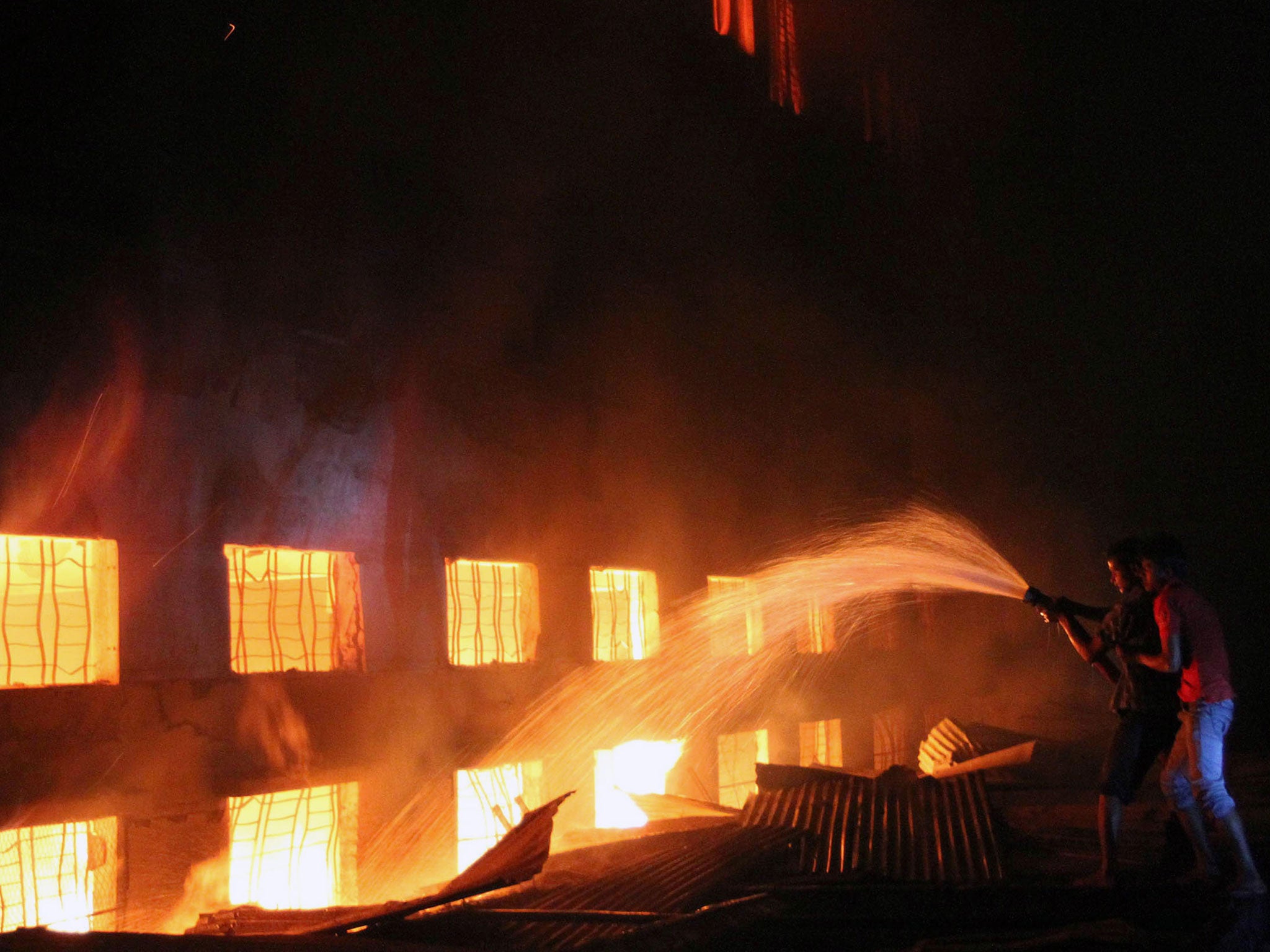 Bangladeshi people and firefighters trying to extinguish a fire in a garment factory