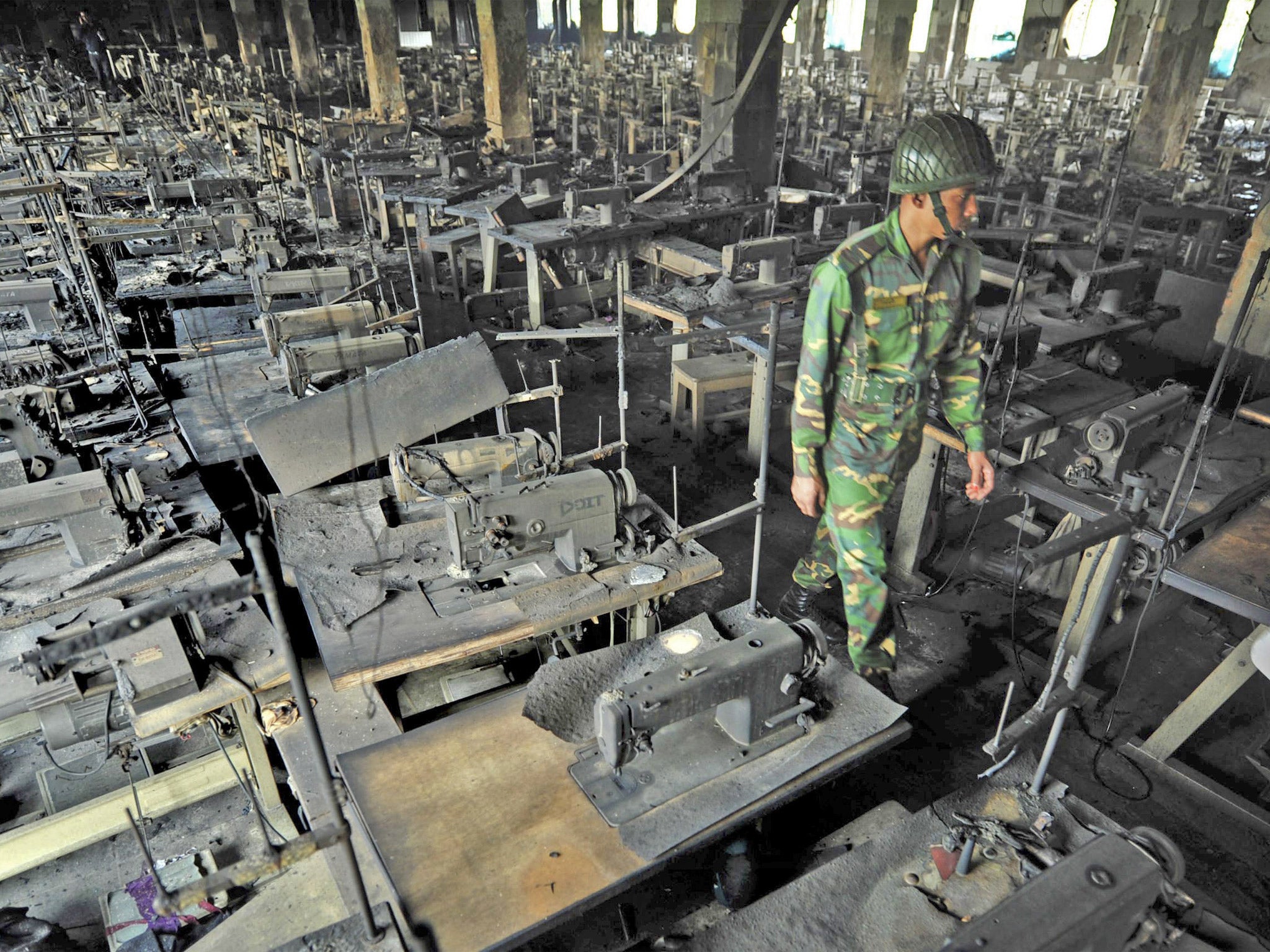 A Bangladeshi police officer walks between rows of burnt sewing machines in a garment factory outside Dhaka, Bangladesh
