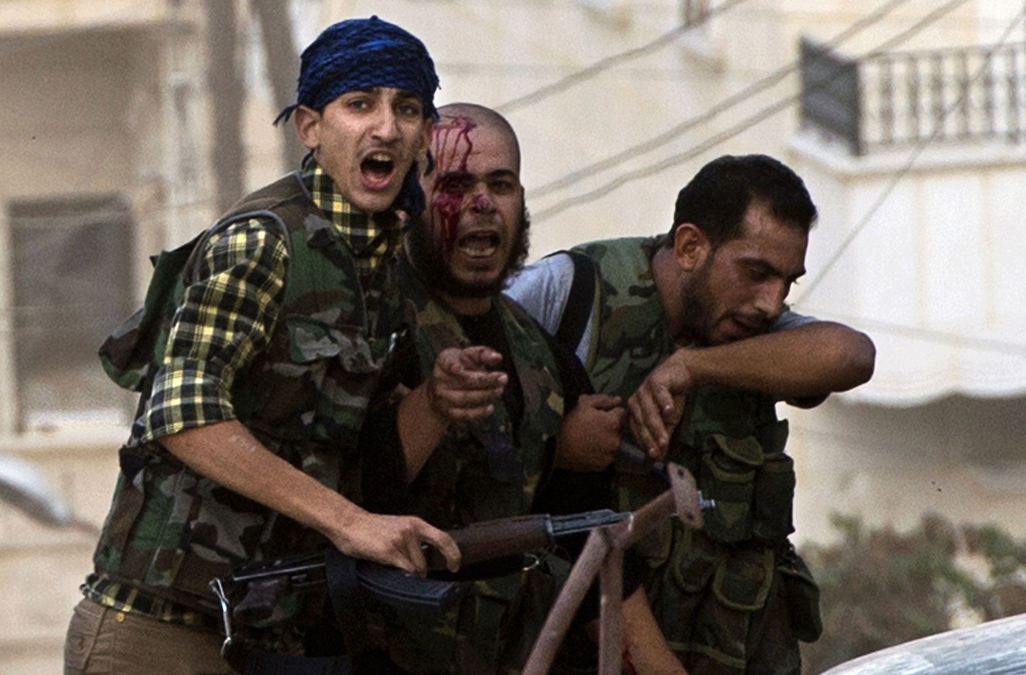An injured rebel fighter is helped during heavy fighting with Syrian government troops