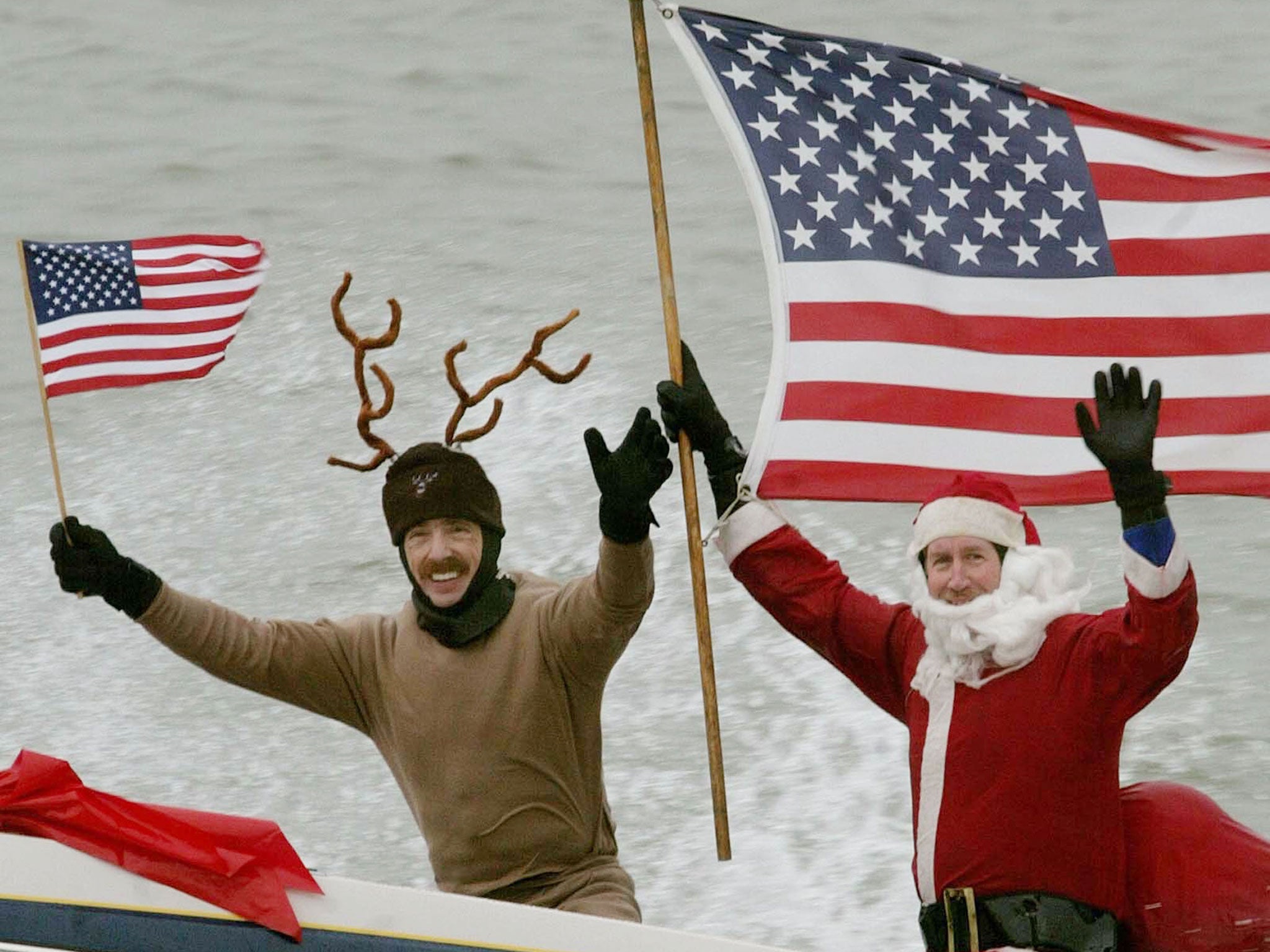 Dressed as Santa Claus, Kerry Nistel (R) holds an American flag after water-skiing along the Potomac River near the Washington Monument December 24, 2003 in Arlington, Virginia.