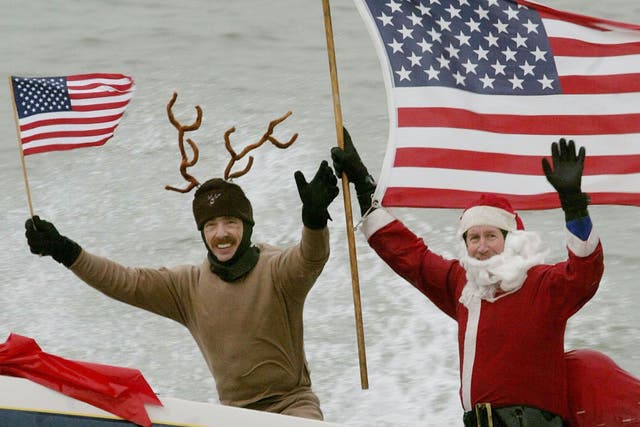 Dressed as Santa Claus, Kerry Nistel (R) holds an American flag after water-skiing along the Potomac River near the Washington Monument December 24, 2003 in Arlington, Virginia.