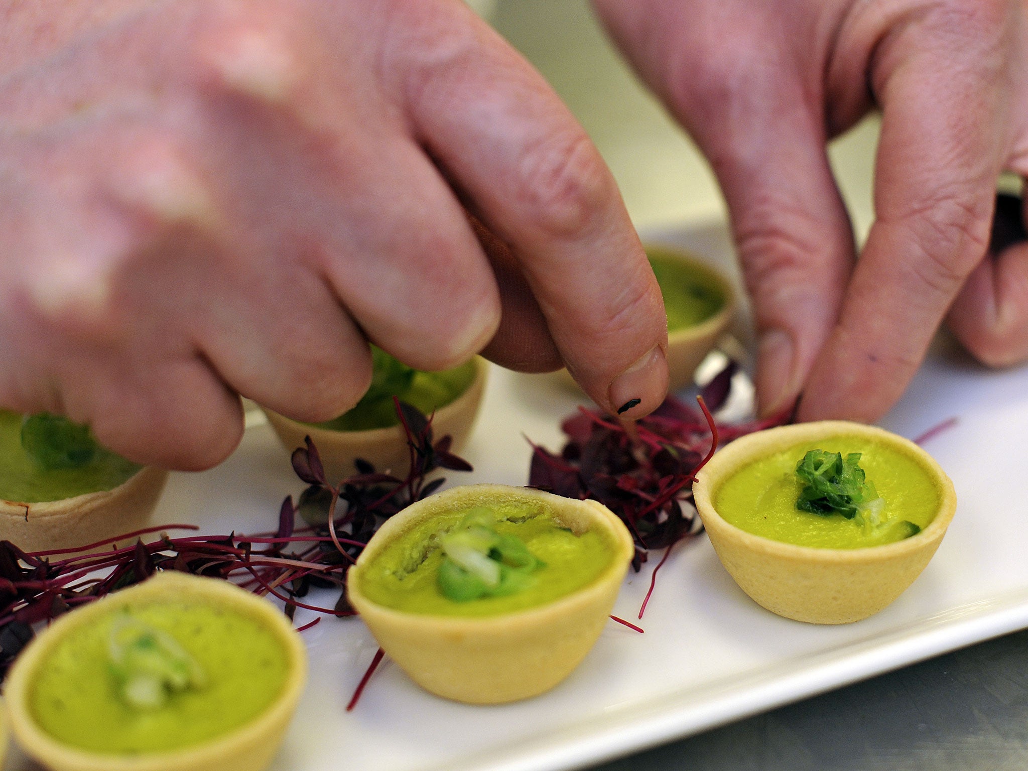 A royal chef adds the finishing garnish to a platter of Wilted Spring Onion and Water Cress quiche canapes, on March 25, 2011 in London, England
