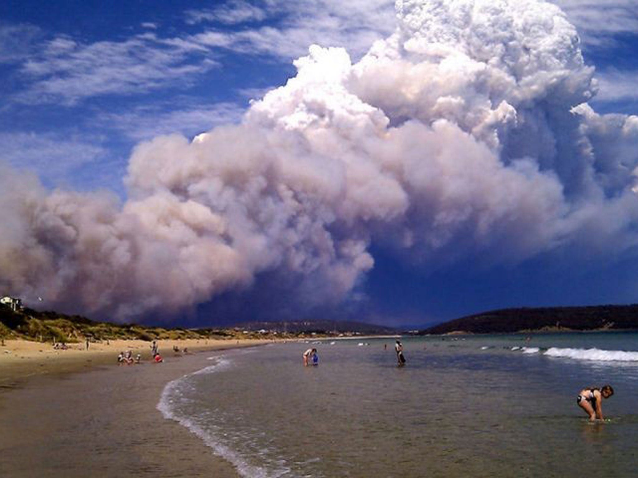 Smoke from a bushfire billows over beach goers at Carlton, about 20 kilometres (12 miles) east of Hobart