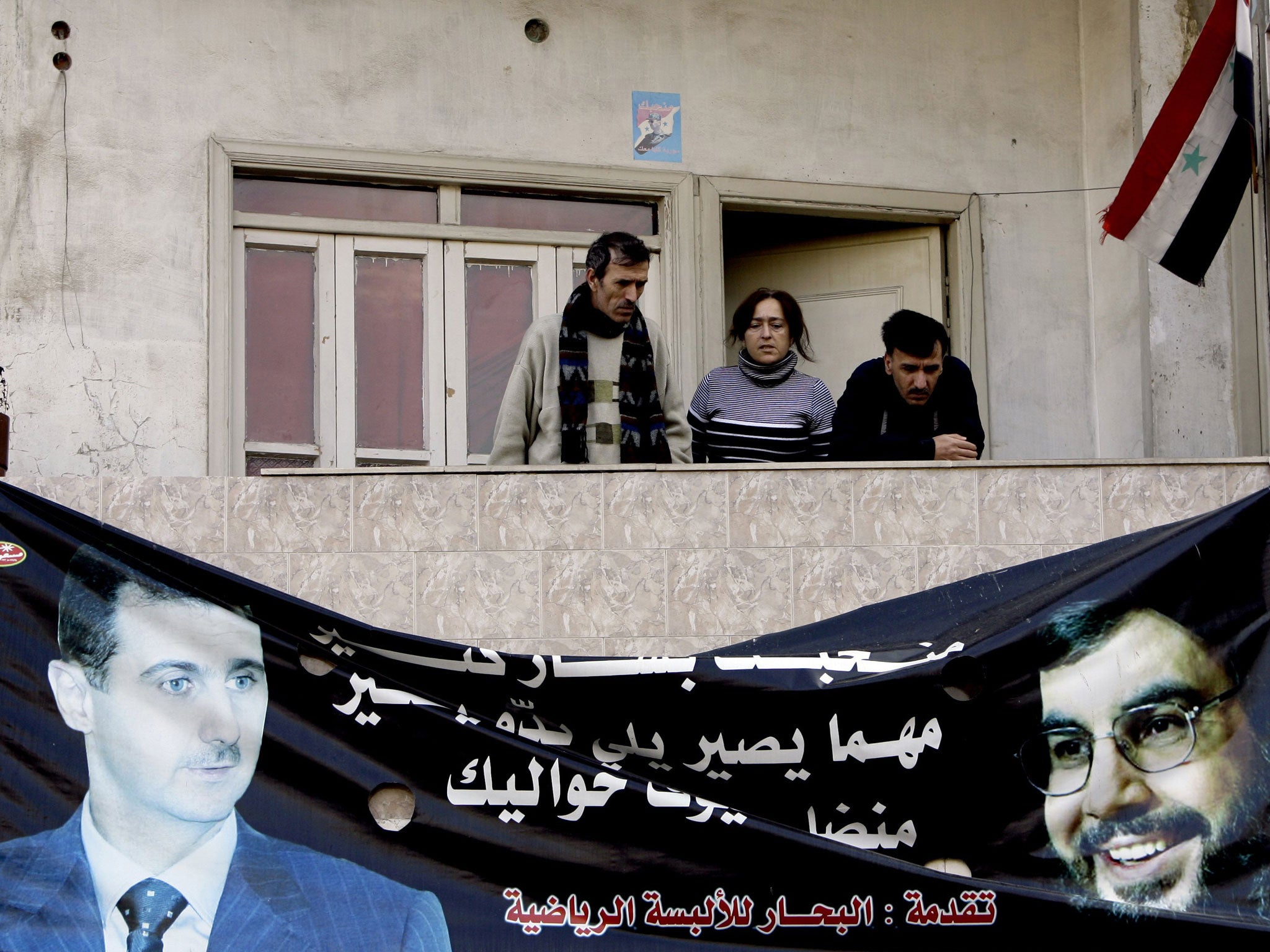 Syrians stand above a poster of Syrian President Bashar al-Assad (L) and Lebanese Hezbollah Leader Hassan Nasrallah (R) hanging on the wall of a building in the Alawite neighbourhood of Nuzhah in the western city of Homs, 162 kms north of Damascus, on January 11, 2012.