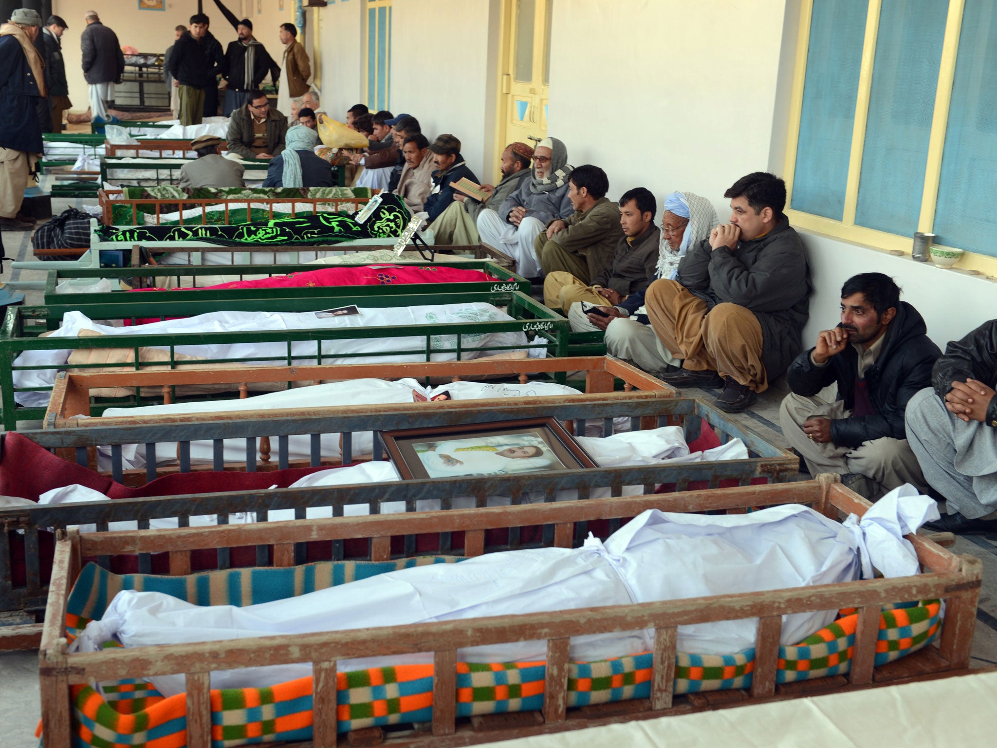 Pakistani Shiite Muslim mourners sit beside the coffins of blast victims