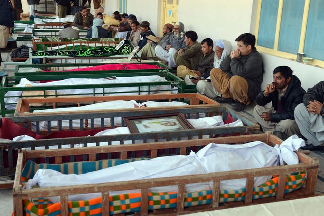 Pakistani Shiite Muslim mourners sit beside the coffins of blast victims