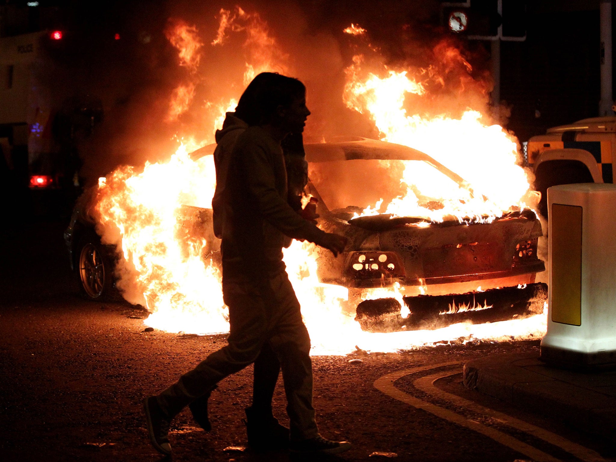 Two girls walk past a car left burning after violence involving loyalists, republicans and police in Belfast yesterday