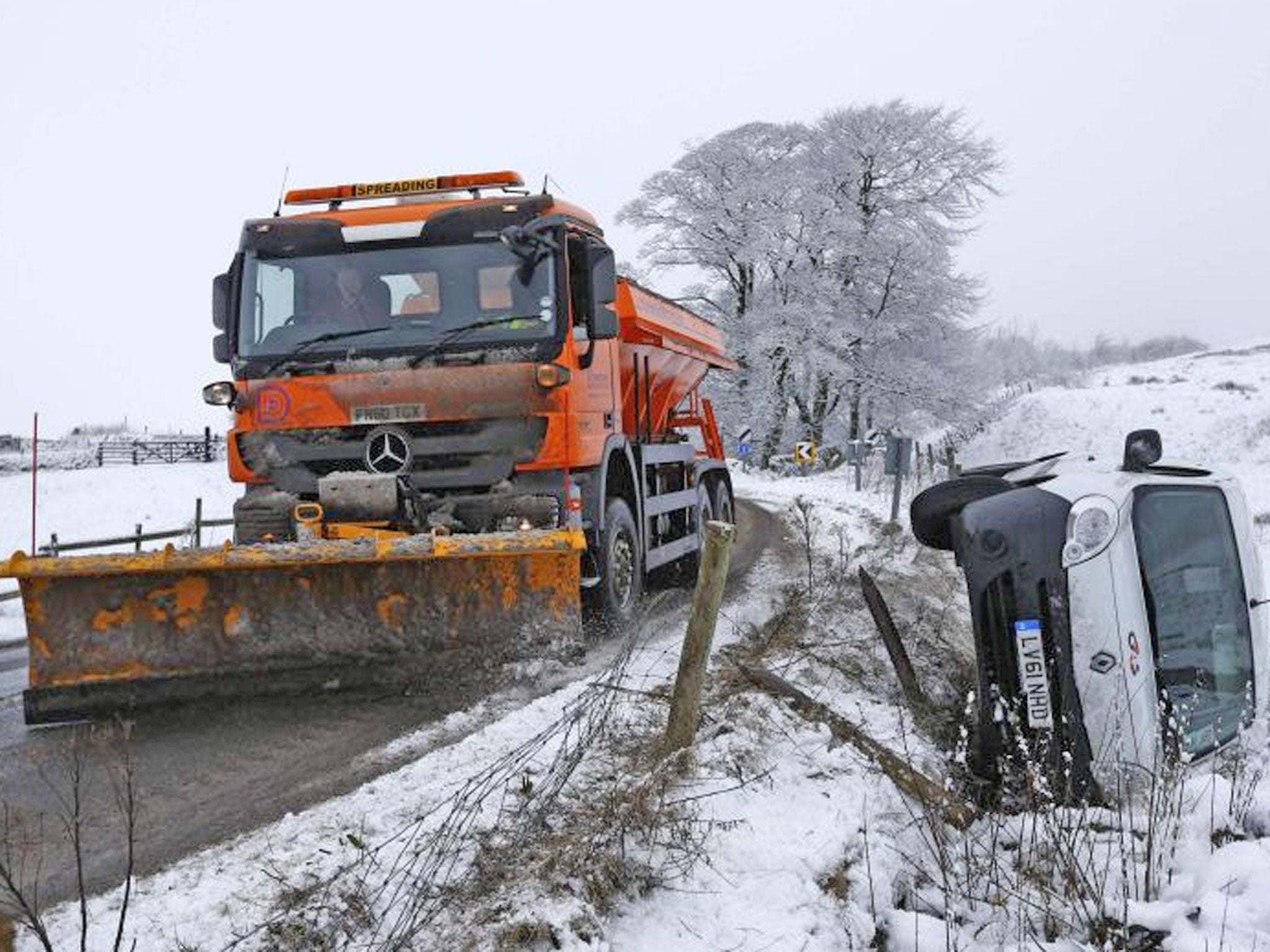 A snow plough is driven past a van crashed in a ditch during snowy weather in Buxton