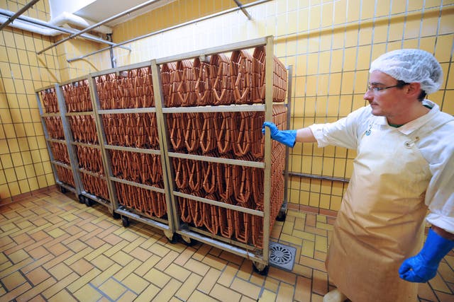 An employee puts sausages placed in carts in an oven prior to be cooked in a sausage processing line