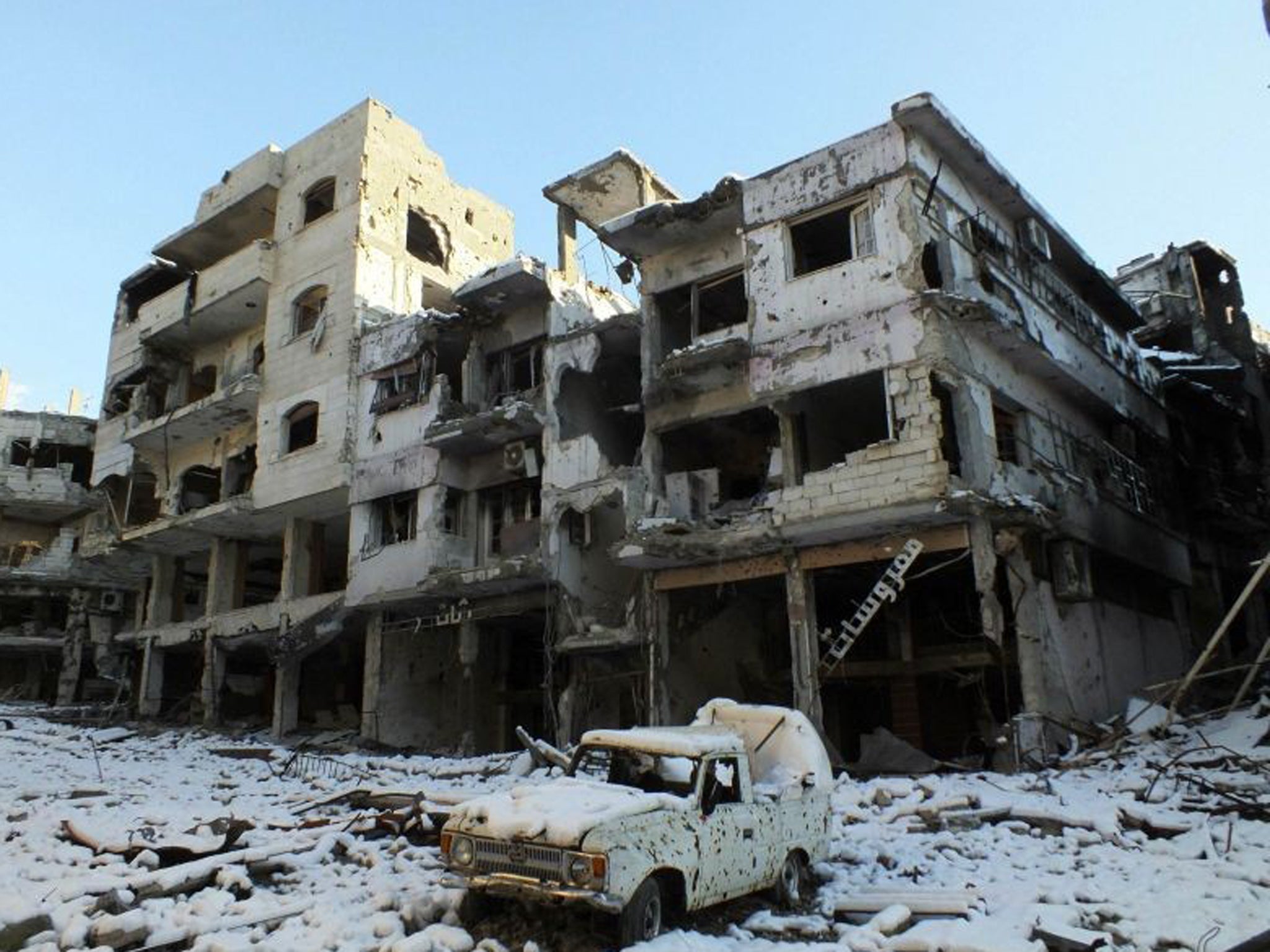 A damaged car and buildings covered with snow are seen at Jouret al Shayah area in Homs