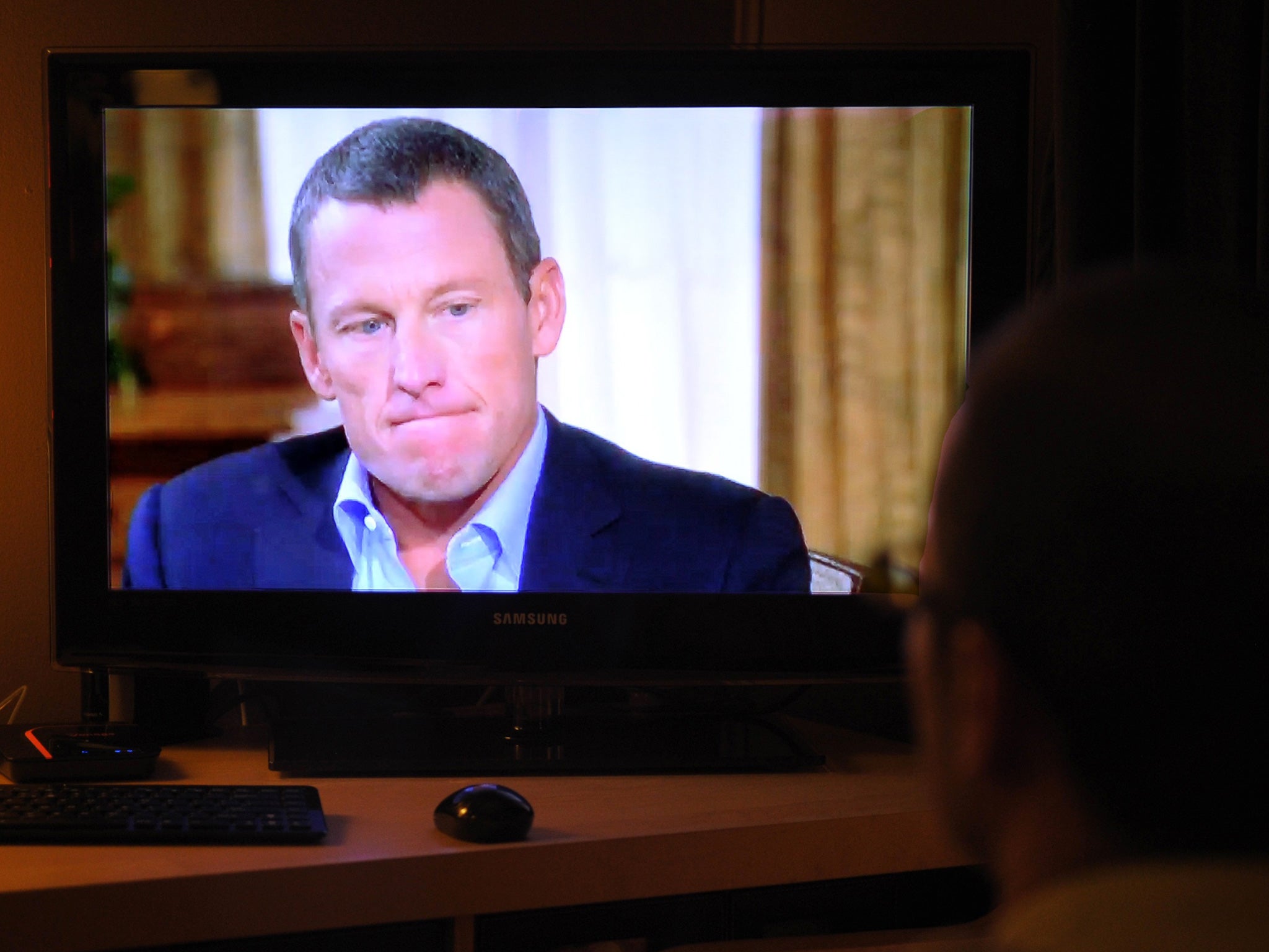 A man watching a TV showing disgraced cycling star Lance Armstrong being interviewed by Oprah Winfrey