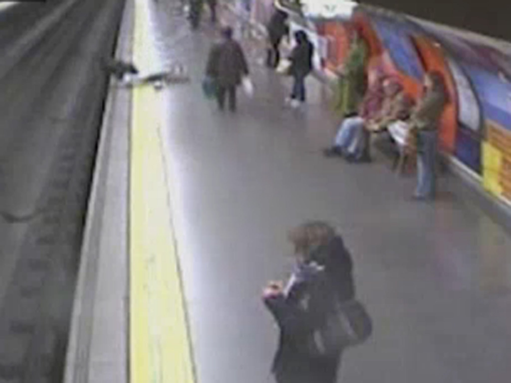 A woman faints on the yellow line shortly before falling onto the tracks