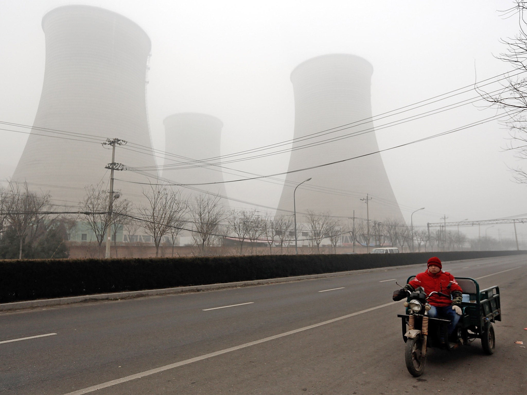 A men rides a three-wheeled motorcycle past power station chimneys. Heavy industry is the main cause of the pollution