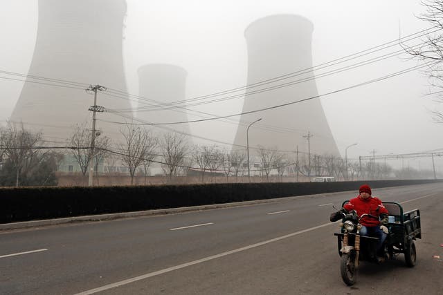 A men rides a three-wheeled motorcycle past power station chimneys. Heavy industry is the main cause of the pollution