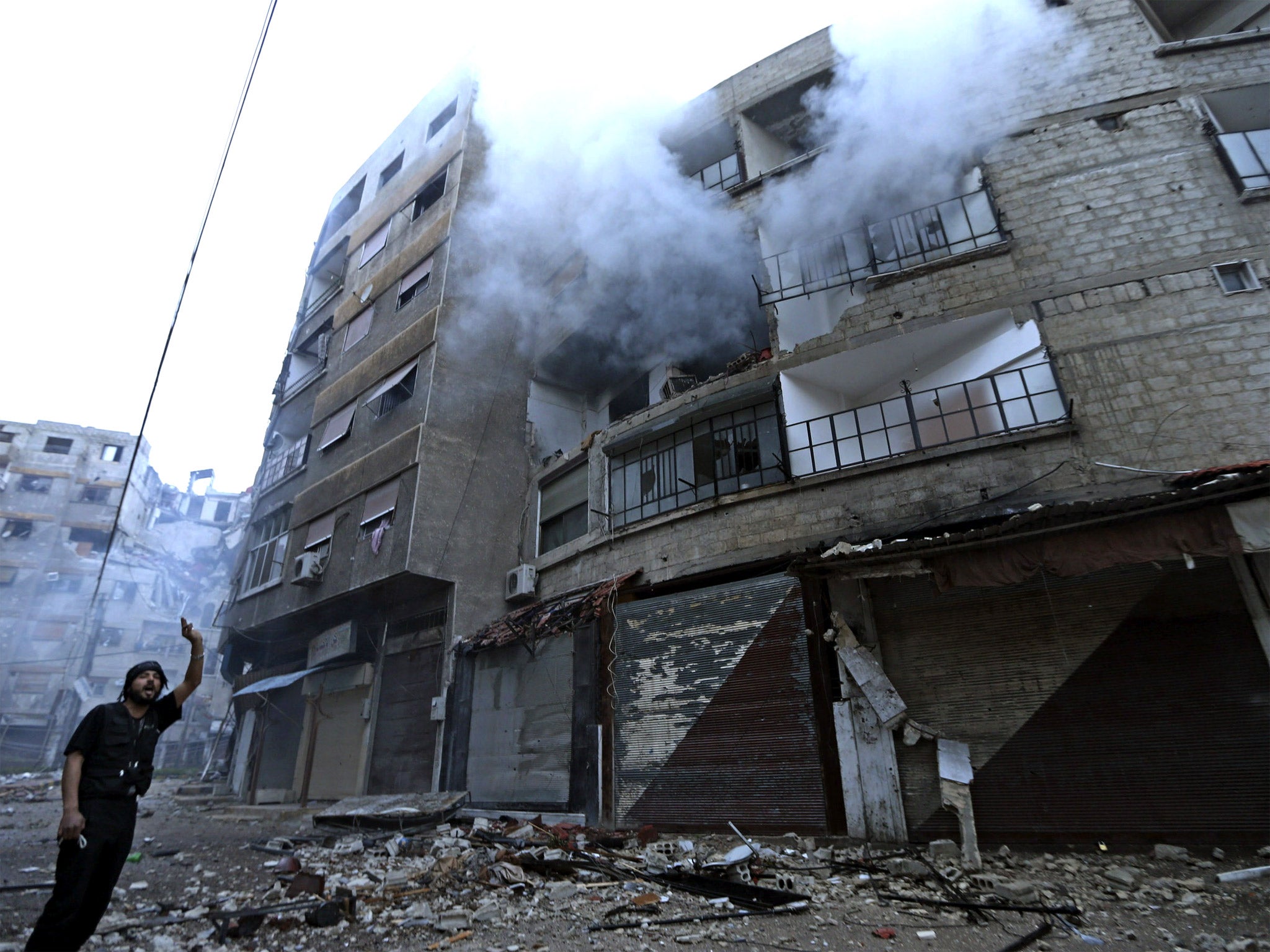 A Free Syrian Army fighter gestures in an empty street in front of a burning building hit by a mortar shell fired by Syrian Army soldiers in the Zamalka neighbourhood of Damascus