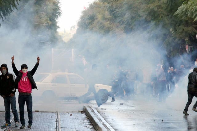 A Tunisian protester gestures as he stands with a fellow demonstrator amid a fog of tear gas fired by police
